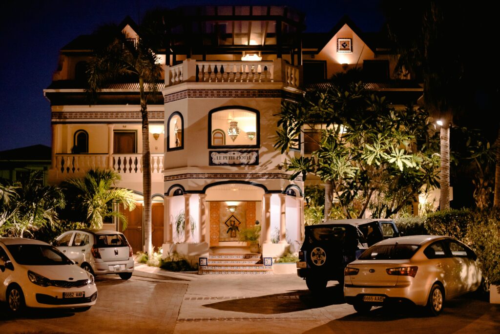 Illuminated villa facade with parked cars at night, showcasing architecture and luxury.