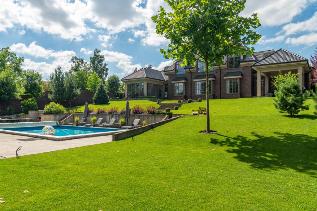 Spacious elegant mansion with a pristine pool, lush garden, and clear blue sky.